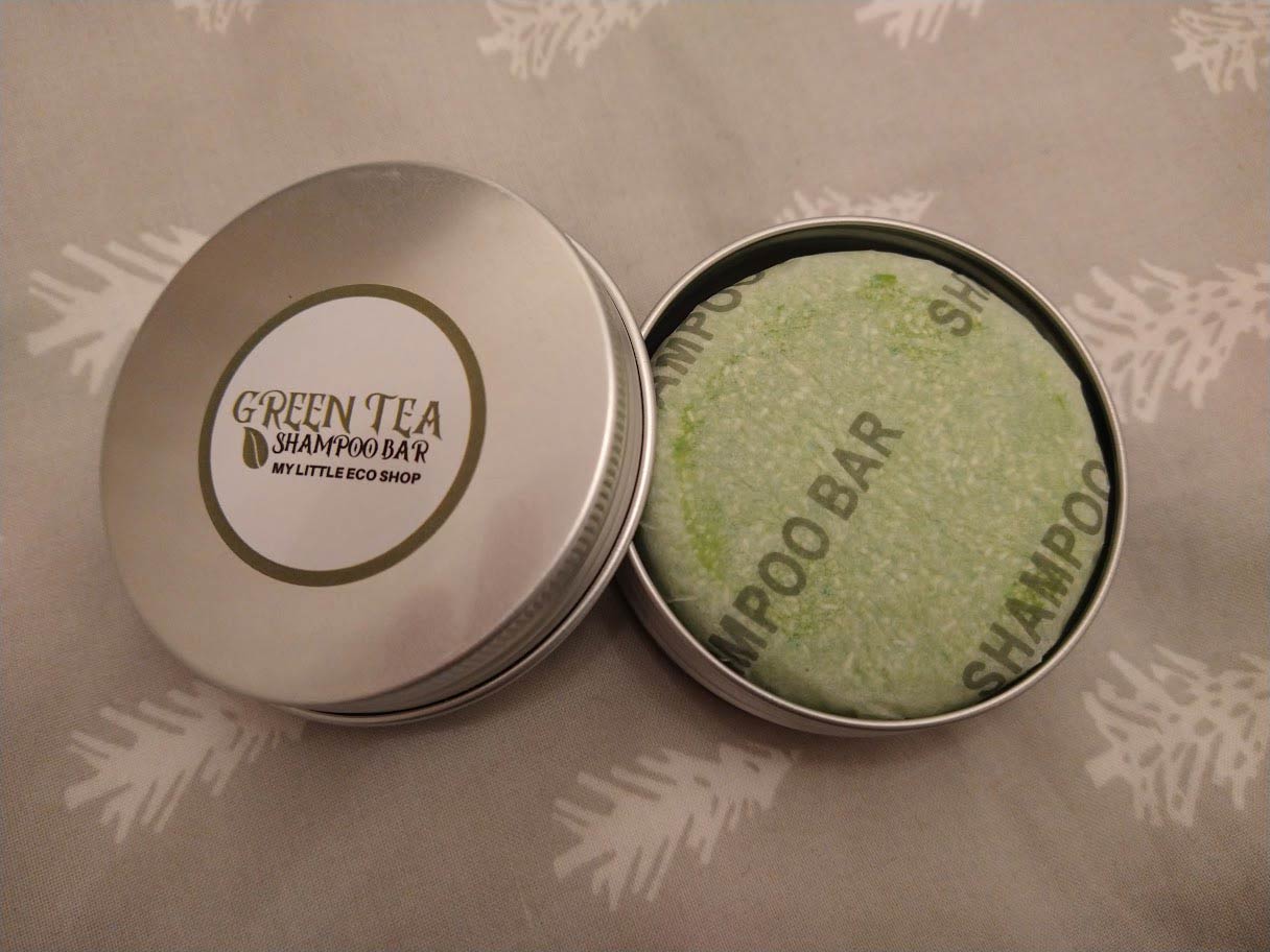The My Little Eco Shop's green tea shampoo bar wrapped in paper and in a tin.