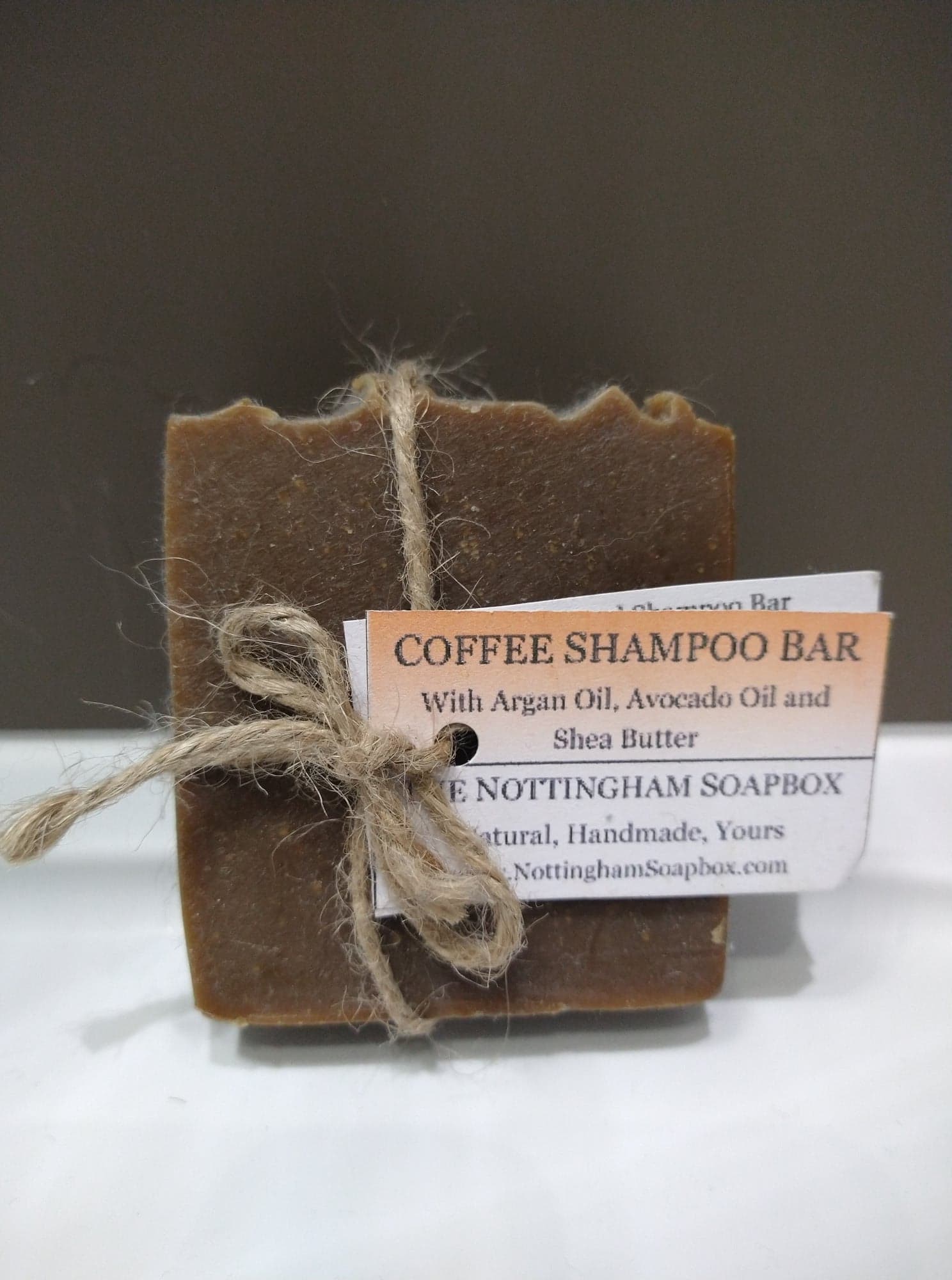 A brown block of Nottingham Soapbox coffee shampoo bar, with a string bow and label.