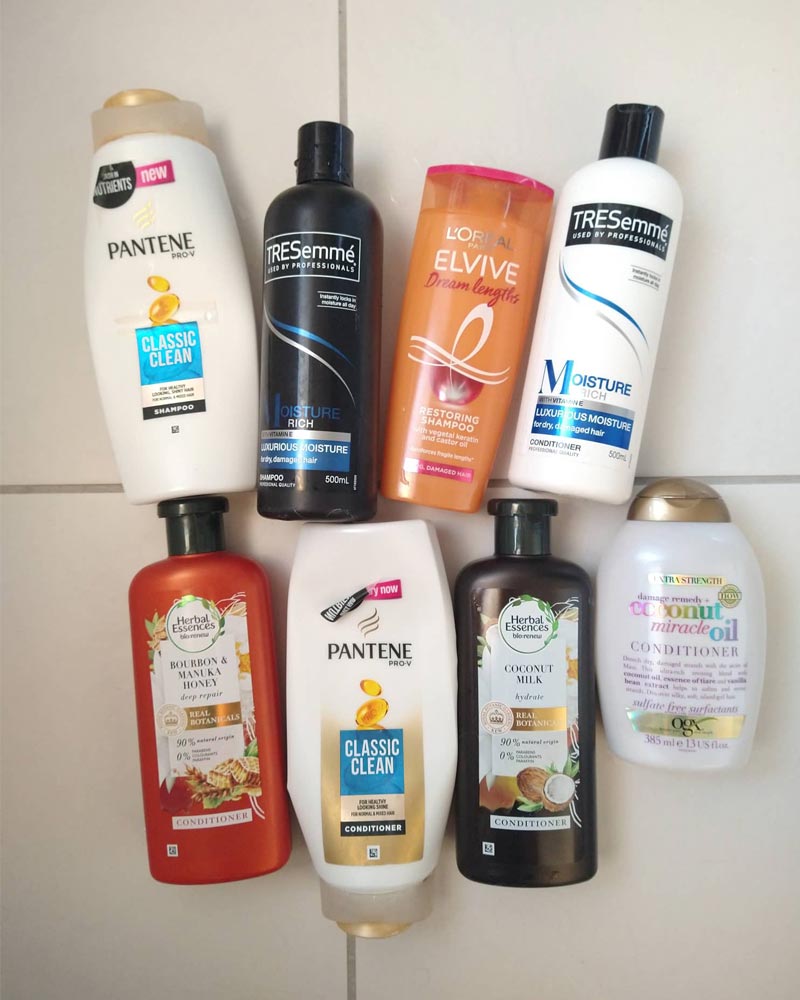 Eight shampoo and conditioner plastic bottles from brands including Pantene, Herbal Essences, and TRESemme.
