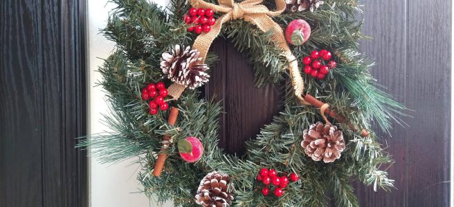 A Christmas wreath complete with red berries, pine cones and cinnamon sticks and hanging from a front door.