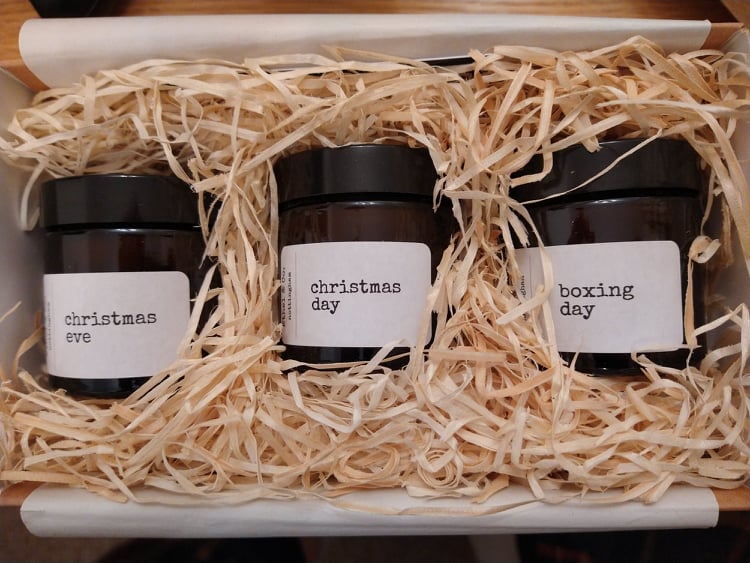 Three eco-friendly jar candles in a box full of shredded paper, labelled, 'Christmas Eve', 'Christmas Day', and 'Boxing Day'.