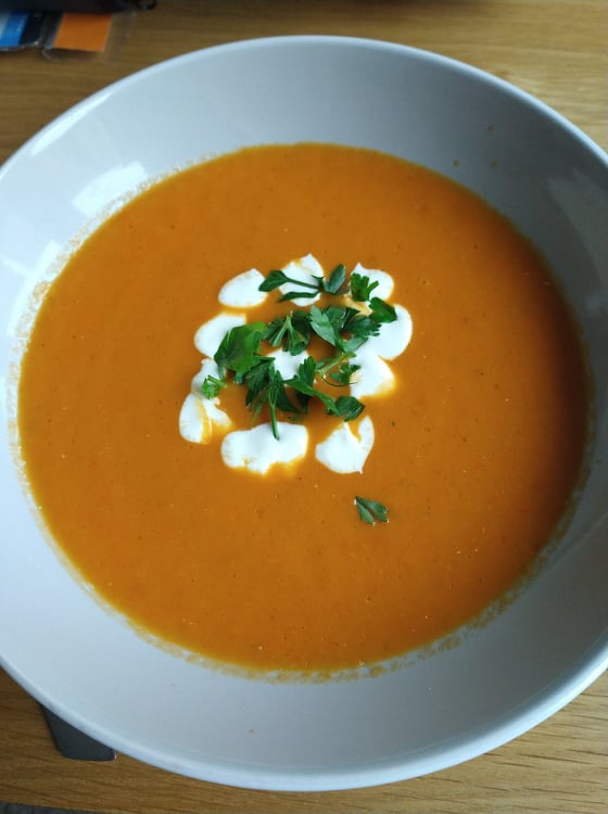 A homemade roasted red pepper soup with blobs of creme fraiche and coriander leaves in the centre.