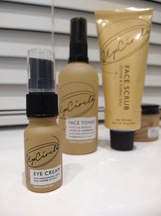 Upcircle's eye cream in a small peach glass bottle, in front of the bottle of face toner and aluminium tube of face scrub.