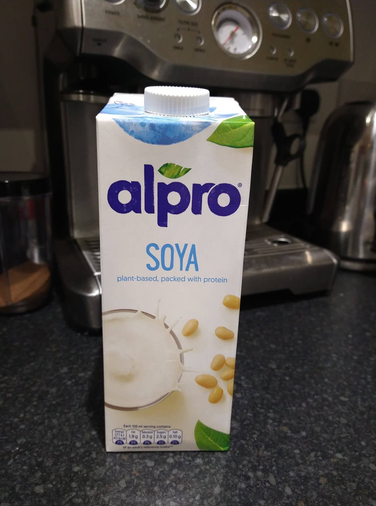A white carton of Alpro soya milk in front of our Sage coffee machine.