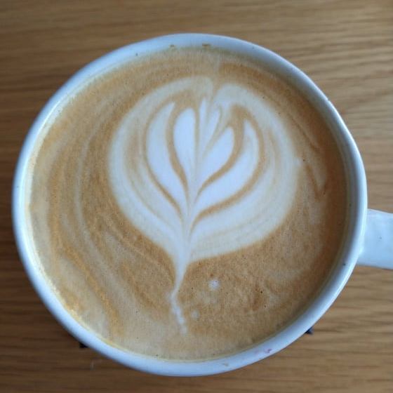 A cup of coffee made with oat milk, and a floral foam art pattern on top.