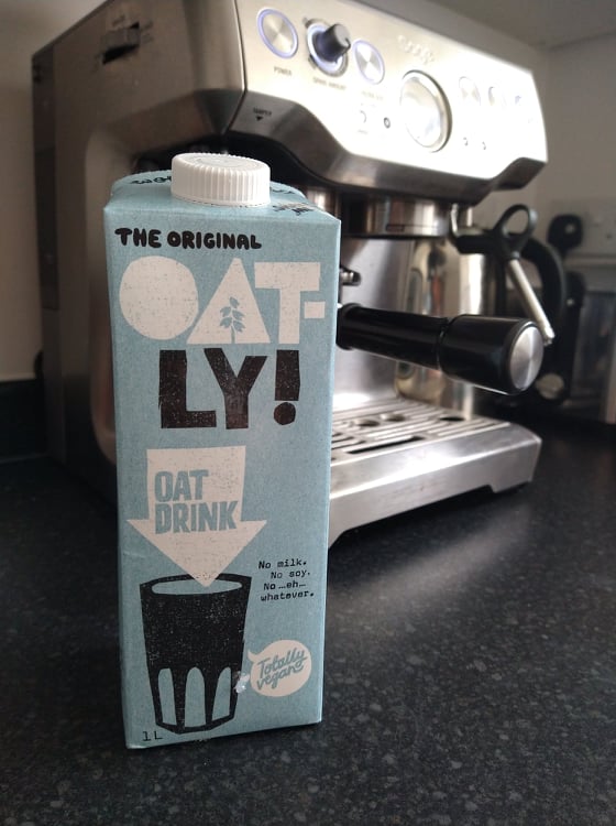 A blue carton of Oatly oat milk, with our  Sage coffee machine in the background.