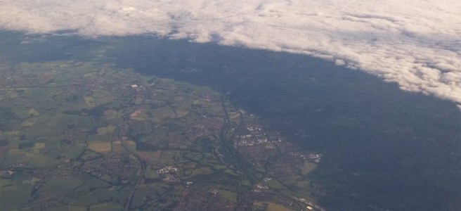 A view of green fields from a plane window, with an ominous cloud sweeping in.