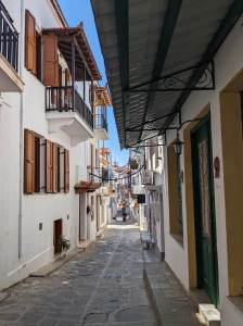 A Greek island street complete with cobbled pavement, wooden shutters and wrought iron balconies on whitewashed buildings.
