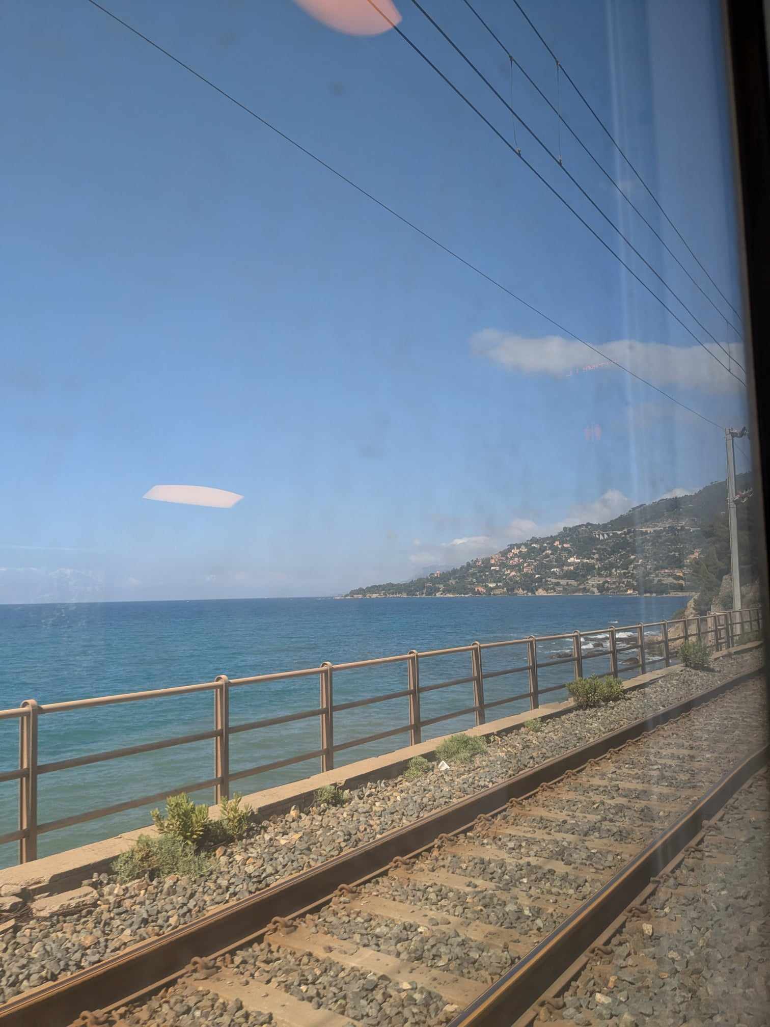View from a train window of the ocean and a peninsula of land with Mediterranean buildings.