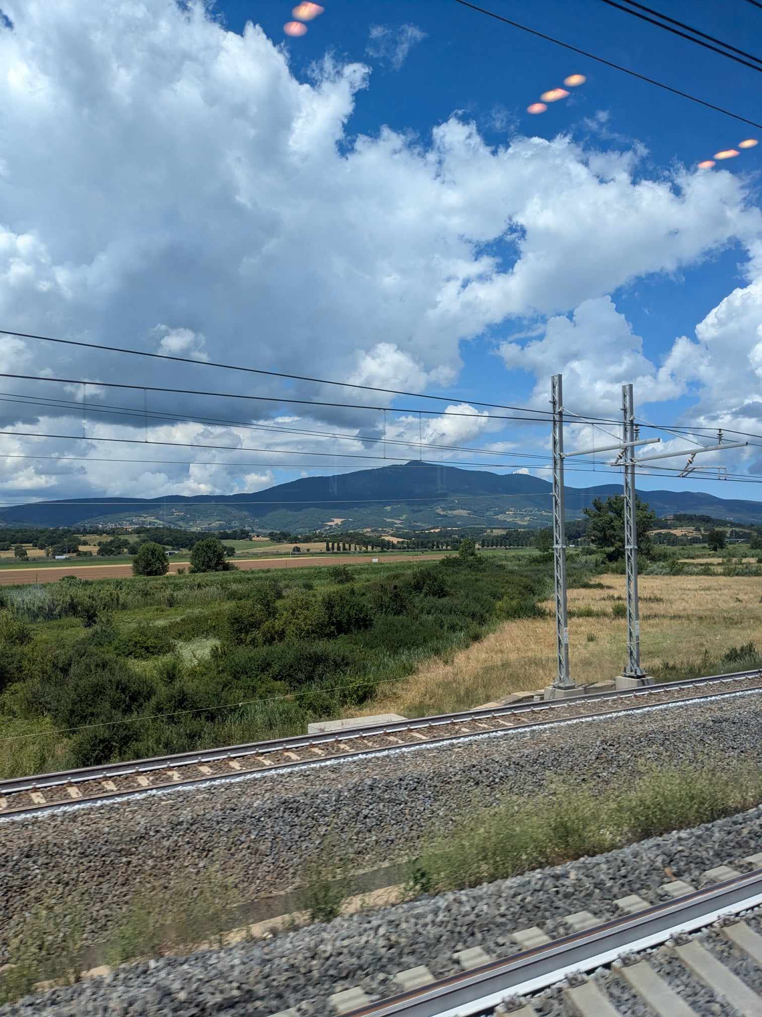 Italian countryside with hills and lush greenery beyond the train tracks.