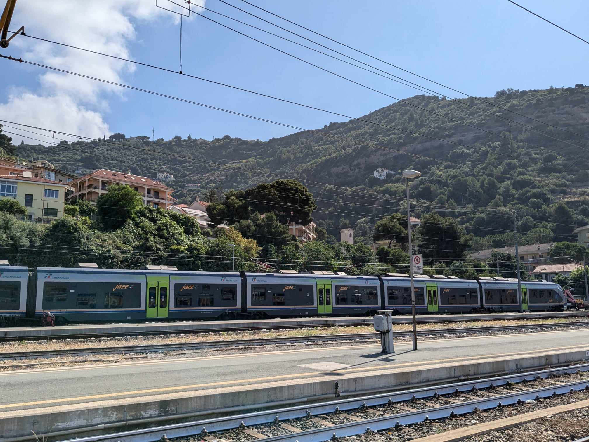 A train pulled into Ventimiglia station, with a backdrop of lush green hills.