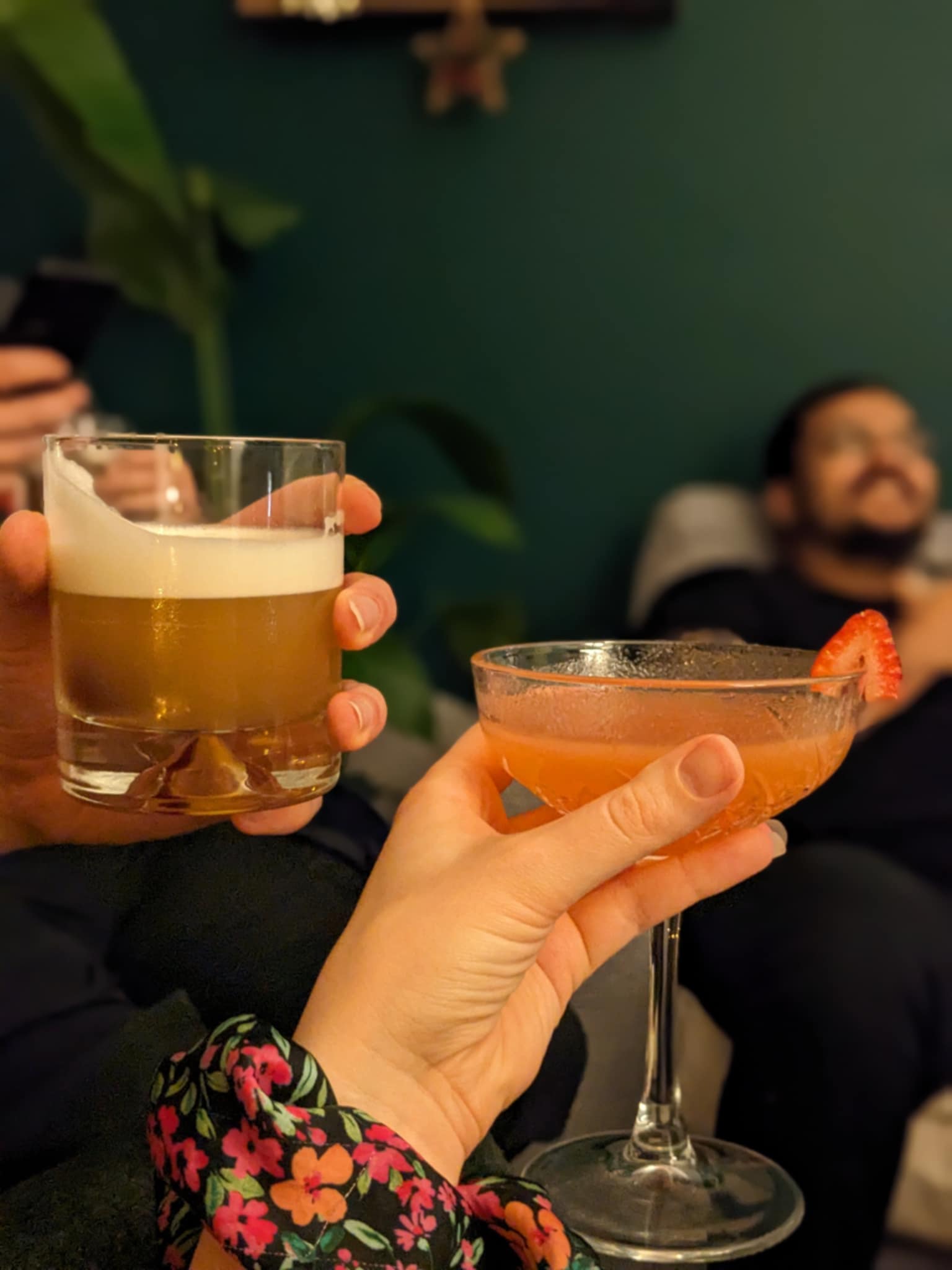 Two hands cheers-ing a homemade amaretto sour and strawberry daiquiri.