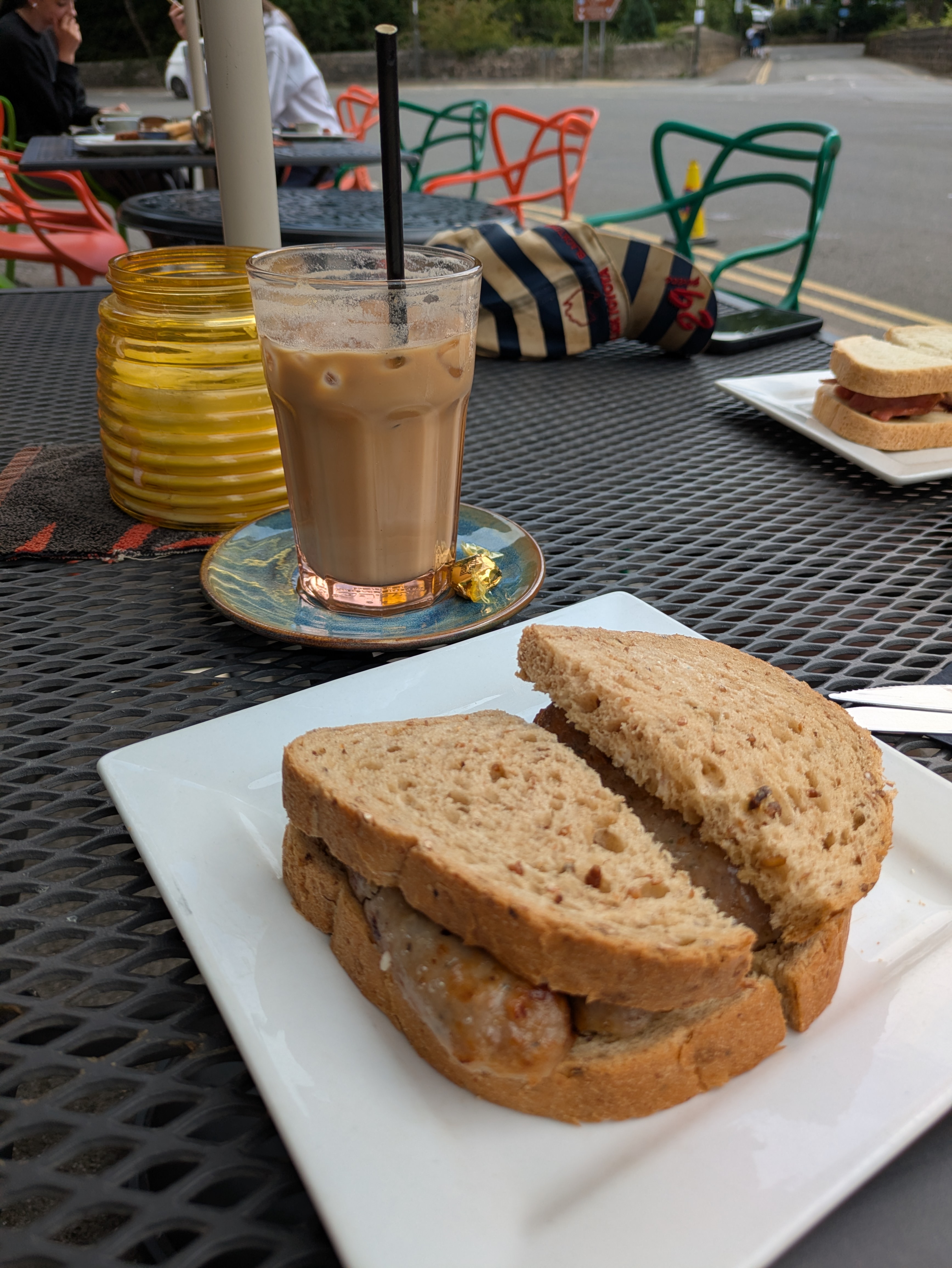 The sausage sandwich on granary bread and an iced latte, sat on a table outside beside the main road.